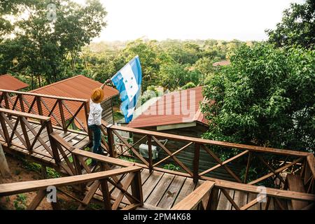 Der Mann, der auf der Promenade steht und die Flagge von Honduras gegen das üppige Grün schwenkt. Stockfoto