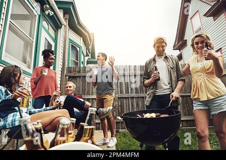 Die größten Freuden des Lebens - Freunde und Essen. Eine Gruppe von Freunden, die ein Barbecue im Hof veranstalten. Stockfoto