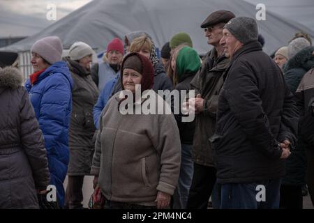 31. März 2023, Oblast Charkiv, Ukraine: Die Menschen warten in einer Warteschlange auf die Verteilung humanitärer Hilfe im Zentrum des Dorfes Zsyrkuny. Die Region Charkiv und der nördliche Teil der Stadt haben unter der russischen Invasion schwer gelitten. Am ersten Tag des Krieges besetzten russische Truppen die umliegenden Dörfer, überraschten die Bewohner und gaben ihnen keine Fluchtmöglichkeit. Die Besetzung dauerte 2,5 Monate, während der viele Einwohner getötet und Gebäude und Infrastruktur zerstört wurden. Trotz fast eines Jahres seit seinem Ende ist das Gebiet aufgrund seiner Nähe zu Russland nach wie vor gefährlich. Surviv Stockfoto