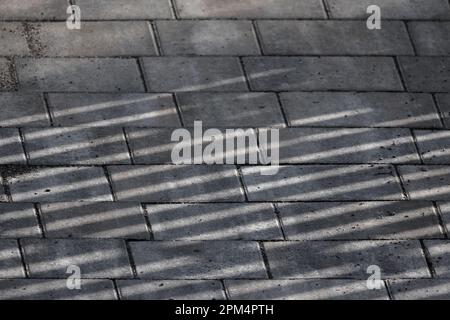 Graue Kopfsteinpflasterstraße aus Beton mit gestreiften Schatten, Hintergrund aus Pflasterplatten Stockfoto