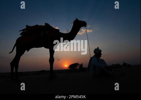 Thar Desert, Rajasthan, Indien- 15.10.2019 : Silhouette des alten Kameliers und seines Kamels in den Sanddünen. Wolke mit untergehender Sonne, Himmelshintergrund. Cameleer Stockfoto