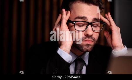 Müde, erschöpfter Mann, Büroangestellter, Manager oder Freiberufler, der an seinem Schreibtisch sitzt und es satt hat, in einem Laptop zu arbeiten Stockfoto