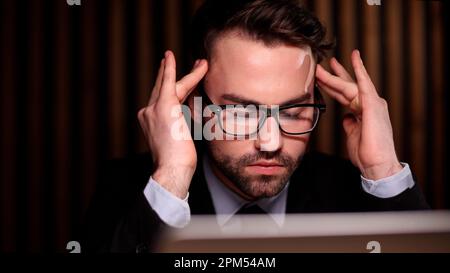 Müde, erschöpfter Mann, Büroangestellter, Manager oder Freiberufler, der an seinem Schreibtisch sitzt und es satt hat, in einem Laptop zu arbeiten Stockfoto