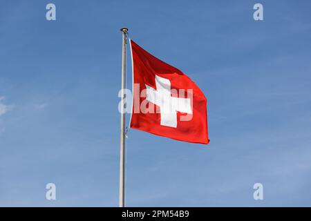 schweizer Flagge im Wind vor einem blauen Himmel Sonne am Tag. Leichte Schleier-Wolken. Direkte Demokratie und Freiheit. Sonnenschein am Tag ohne dich Stockfoto