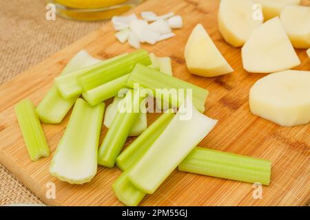 Rohes Gemüse wie Selleriestangen, Kartoffeln, gehackte Zwiebeln, Nahaufnahme auf dem Küchentisch. Zutaten für ein Selleriesuppen-Rezept Stockfoto