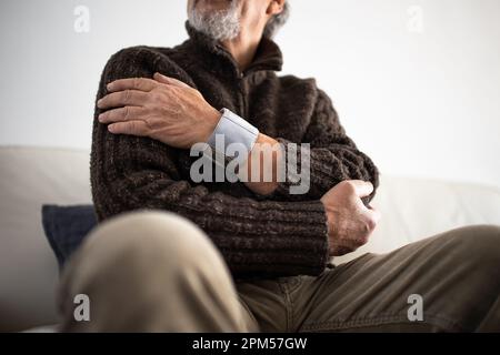 Seniormann, der ein medizinisches Gerät zur Blutdruckmessung verwendet - Älterer Mann, der an Bluthochdruck leidet, sitzt zu Hause auf dem Sofa und kümmert sich um seine h Stockfoto