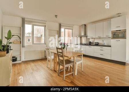 Küche und Essbereich in einem kleinen Apartment mit Holzfußboden, weißen Schränken und einem Ofen an der Wand Stockfoto