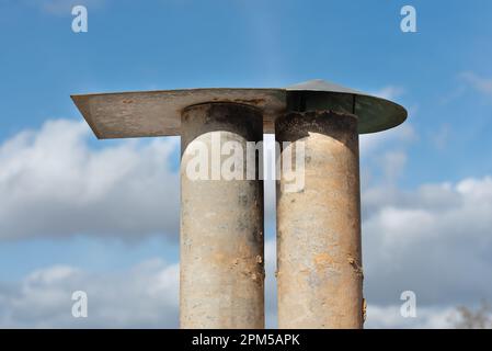 Nahaufnahme eines alten Schornsteins vor einem blauen Himmel. Der Kamin besteht aus zwei Rohren, die durch ein Dach geschützt sind. Stockfoto