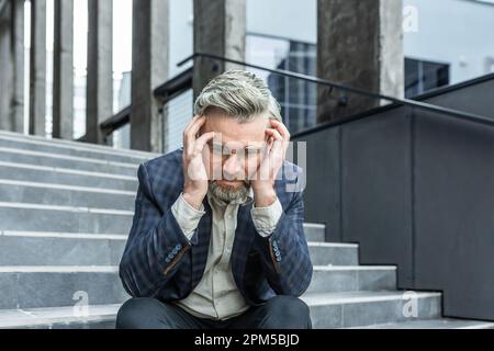 Ein Mann im Anzug sitzt vor dem Gericht auf der Treppe und schaut nach unten, hält seinen Kopf in den Händen. Vorsätzlich, stressig. Scheidung, Unterhalt, Strafverfahren, finanzielle Probleme. Stockfoto