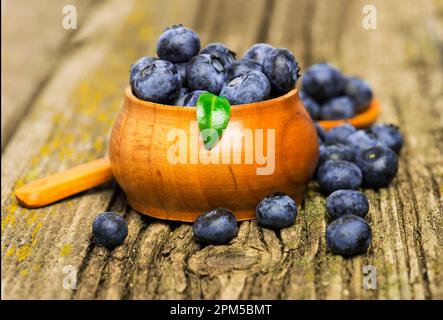 Frische Bio-Blaubeeren mit Blättern in der Schüssel auf Holzhintergrund. Stockfoto