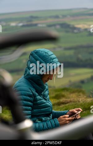 Eine Frau, die ihr Telefon benutzt und am Strand sitzt Stockfoto