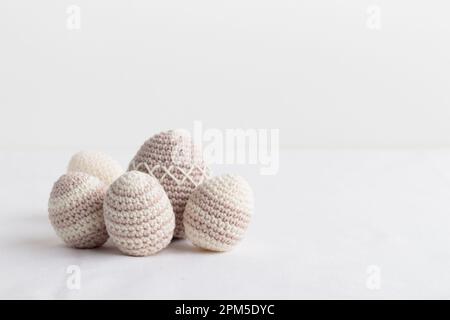 Set mit süßen handgestrickten Eiern, pastellfarben auf einem weißen Tisch Stockfoto