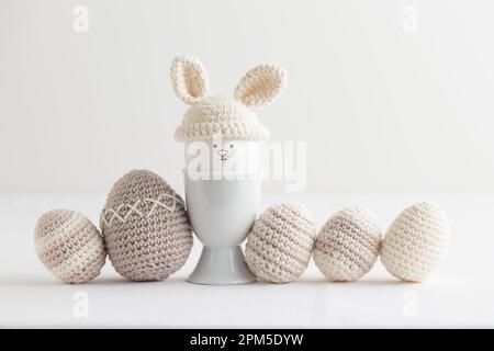 osterei in Häkelmütze mit Hasenohren im Eierhalter auf weiß Stockfoto