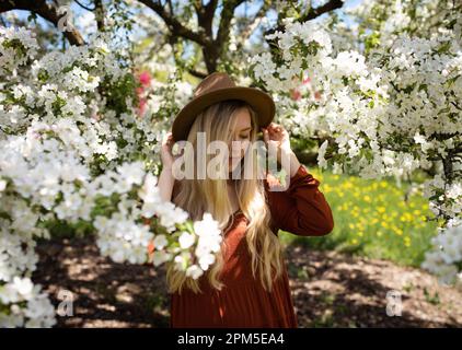 Junge Frau, die nach unten blickt, mit Hut, umgeben von weißen Birnenblumen Stockfoto