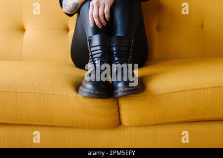 Aus nächster Nähe schwarze Stiefel, Seite an Seite auf die gelbe Couch gezogen Stockfoto