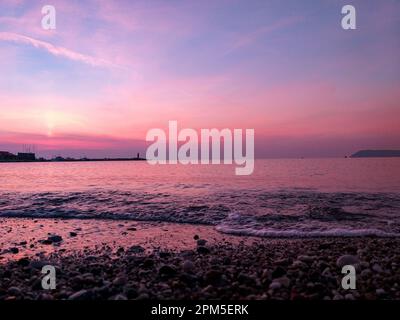 Wunderschöner Sonnenuntergang, farbenfroher Himmel und Leuchtturm auf offenem Meer Stockfoto