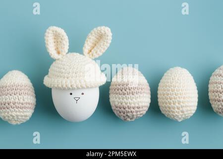 ostereier in Häkelmütze mit Hasenohren auf blauem Hintergrund Stockfoto