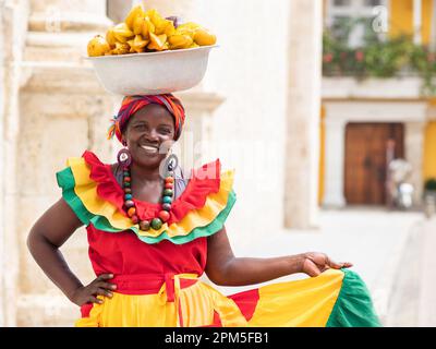 Fröhlicher, lächelnder Palenquera-Straßenverkäufer mit frischem Obst in der Altstadt von Cartagena, Kolumbien. Fröhliche afrokolumbianische Frau in traditionellen Kostümen. Stockfoto