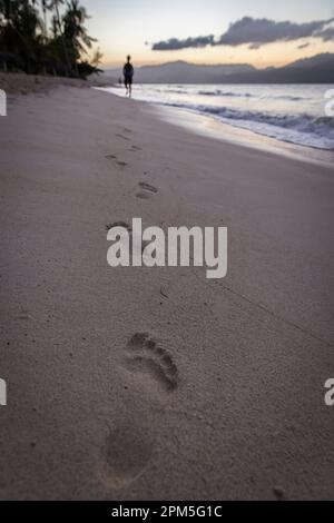Schritte im Sand bei Sonnenuntergang mit Gehhilfe in der Ferne Stockfoto