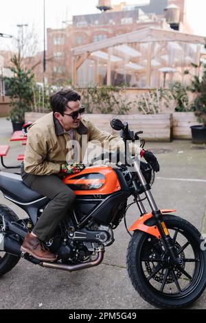 Ein Mann auf einem orangefarbenen und schwarzen Motorrad parkt im Innenhof Stockfoto