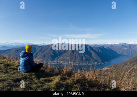 Ein Reisender, der auf dem Berggipfel sitzt und die Landschaft bewundert Stockfoto