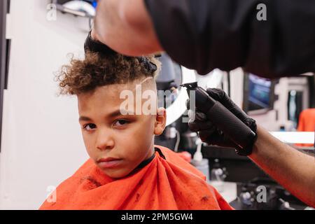 Gemischter Rennjunge mit lockigem Haar bekommt einen frischen Haarschnitt Stockfoto