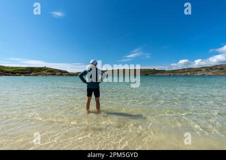 Eine Frau mit ihren Füßen in klarem türkisfarbenem Wasser in Dog's Bay Stockfoto