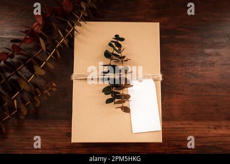 Leerer weißer Geschenkanhänger mit brauner Geschenkbox, Garn, Eukalyptusblättern Stockfoto