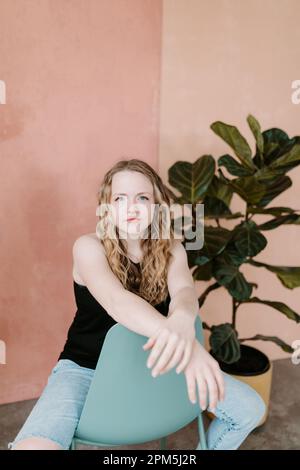 Wunderschöne junge Frau, die direkt in die Kamera starrt und auf einem Stuhl sitzt Stockfoto