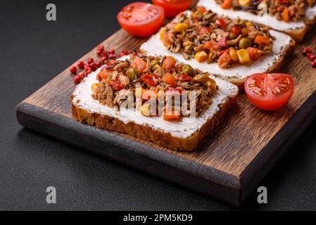 Köstliche vegetarische Sandwiches mit Thunfischkonserven und mexikanischem Mischgemüse auf dunklem Betonhintergrund Stockfoto