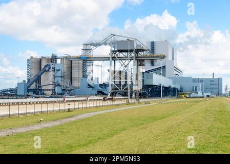 Kohlekraftwerk am Hafen an einem teilweise bewölkten Sommertag. Dichter Rauch stößt aus zwei Schornsteinen heraus. Stockfoto