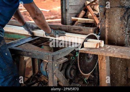 Nahaufnahme einer Kreissäge im Betrieb mit den Händen des Arbeiters und Staub in der Luft. Stockfoto