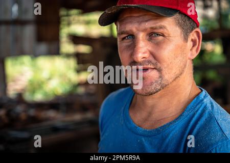 Nahaufnahme eines gutaussehenden männlichen Arbeiters mit rotem Hut, der in die Kamera schaut. Arbeit, Schwerindustrie, Beruf Stockfoto