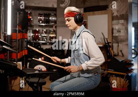 Hipster-Musikerin mit Kopfhörern, die im Musikgeschäft Trommeln spielt Stockfoto