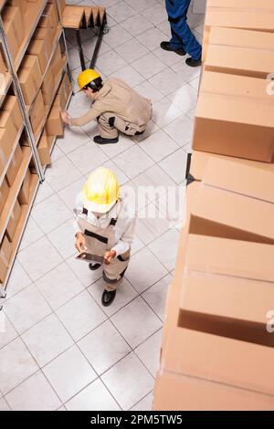 Mitarbeiter im Lieferlager, die Kartonkartons verpacken und das Paket mithilfe der Checkliste auf dem digitalen Tablet durchsuchen. Industrielle Lagerassistenten, die Kundenbestellungen für den Transport vorbereiten Stockfoto