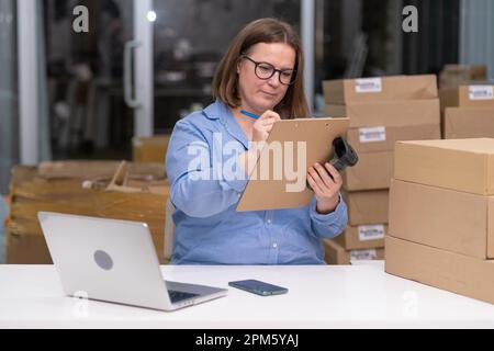 Online-Verkauf an Lagerlieferung: Ein Direktlieferungsunternehmen, woma-Laptop, Prüfung der Versandverpackung, Stockfoto