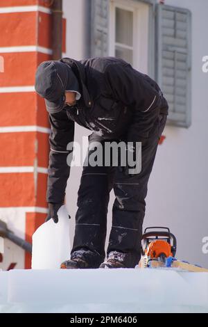 Eisbildhauer, der auf einer Skulptur steht und versucht, ein Stück Eis zu bewegen. Stockfoto