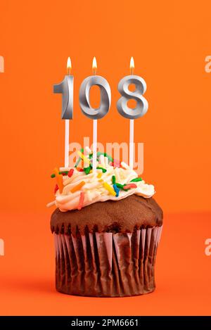 Kerze Nummer 108 - Kuchen zum Geburtstag auf orangefarbenem Hintergrund Stockfoto