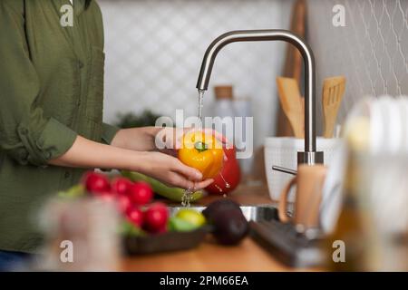 Nahaufnahme von der Seite einer jungen Frau, die frisches reifes Gemüse in der Küche wäscht, Kopierraum Stockfoto