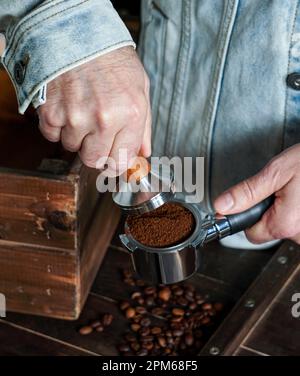 Barista Hold Portafilter und Coffee Tamper bereiten Kaffee in einem Café oder Café mit dunklem Hintergrund zu Stockfoto