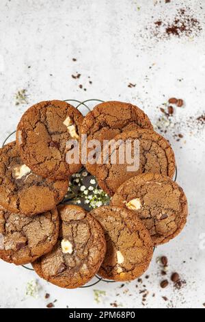 Schokoladen-Chip-Espresso-Kekse in einem Kreis auf einem Drahtgestell mit gemahlenem Kaffee auf der Arbeitsfläche. Stockfoto