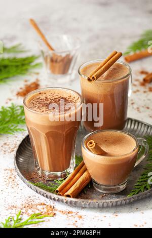 Drei Glasbecher in verschiedenen Größen mit heißer Schokolade und Zimtstangen als Garnierung. Stockfoto