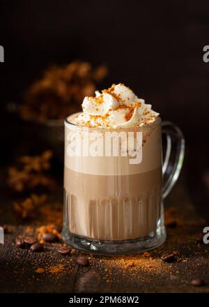 Ein süßes Latte-Kaffeegetränk garniert mit Schlagsahne und Kekskrümeln in einer dunklen und stimmungsvollen rustikalen Umgebung. Stockfoto