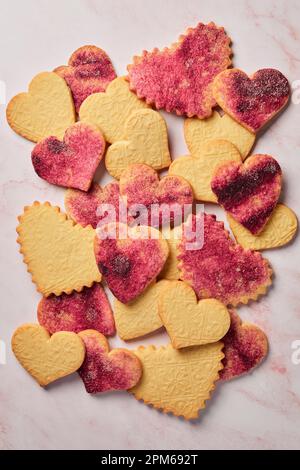 Gestanzte Kekse mit Herzausschnitt und rosafarbenem Zucker auf pinkfarbenem Marmorhintergrund Stockfoto