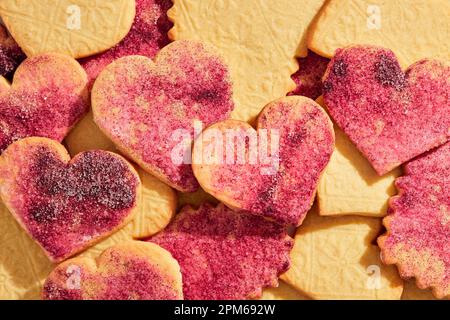 Gestanzte Kekse mit Herzausschnitt und rosafarbenem Zucker auf pinkfarbenem Marmorhintergrund Stockfoto