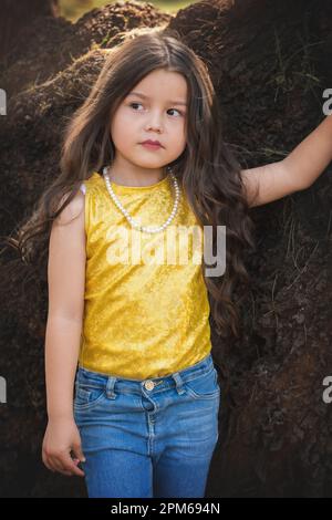 Blondes Mädchen in einer Fotosession, posiert auf einem Baum. Ausdruck des Glücks. Modellmädchen. Kindertag-Thema. Stockfoto