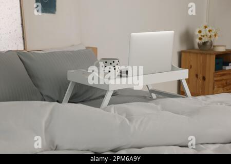 Weißer Tablett-Tisch mit Laptop und eine Tasse Getränk auf dem Bett drinnen Stockfoto