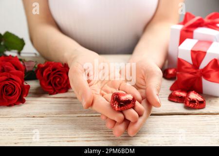 Frau mit herzförmigen Schokoladenbonbons am weißen Holztisch, Nahaufnahme Stockfoto