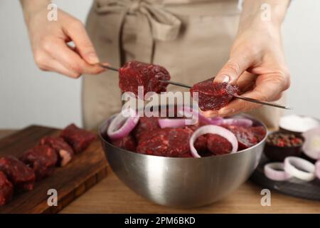 Eine Frau, die mariniertes Fleisch auf einem Spieß auf einem Holztisch aufhängt, Nahaufnahme Stockfoto