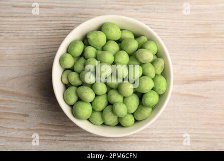 Leckere Wasabi-beschichtete Erdnüsse in der Schüssel auf weißem Holztisch, Draufsicht Stockfoto